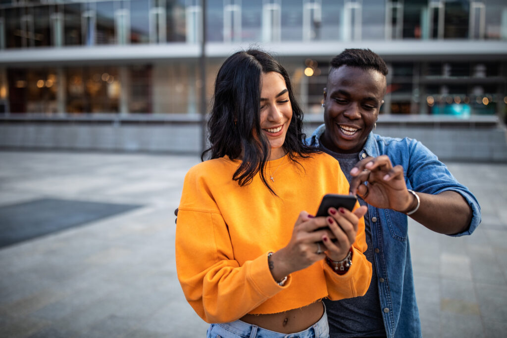 Beautiful, cheerful couple looking at smart phone, choosing the best photo for social media